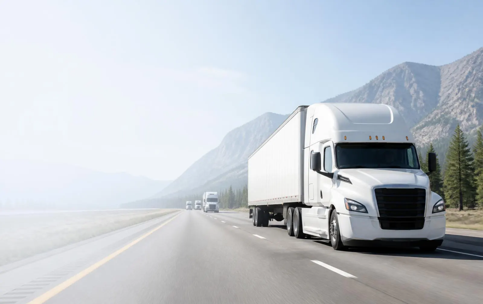 A white semi truck and dry-van fleet traveling on a mountain highway